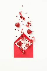 Open red envelope decorated confetti, candy, party streamers on white background. Love, romantic letter concept. Happy Valentines day composition.
