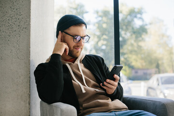 Picture of happy young man holding his cellphone in hands and chatting.