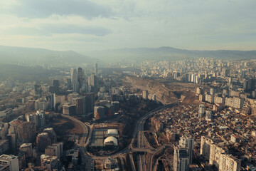 Fototapeta premium Aerial view from drone flying above Tbilisi Georgia city near Vake district with traffic car on road and high tower buildings on hills.