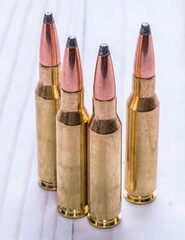 Four bullets used for hunting, two 30.06 caliber and two 7mm-08 caliber together on a white wooden background
