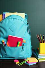 Backpack with different school stationery on white table near chalkboard