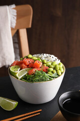 Delicious poke bowl with lime, fish and edamame beans on black table