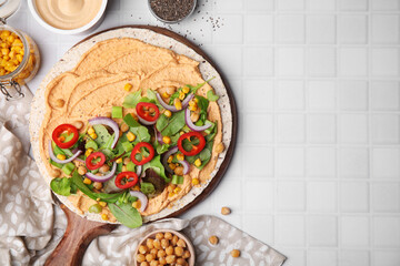 Tortilla with hummus and vegetables on white table, flat lay. Space for text