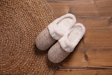 Fototapeta na wymiar Pair of warm stylish slippers and wicker mat on wooden floor, flat lay