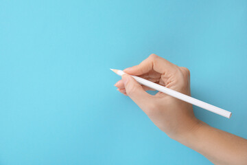 Woman with white pencil on light blue background, closeup. Space for text