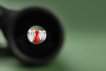 Recruiter searching employee. Red and white pawns visible through binoculars on green background....
