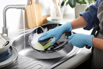 Woman washing dirty frying pan in sink indoors, closeup