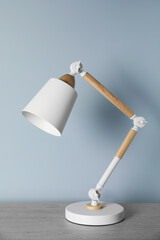 Stylish modern desk lamp on wooden table near white wall