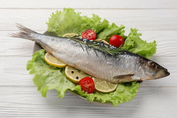 Delicious salted herring, rosemary, lettuce, tomatoes and lemon on white wooden table