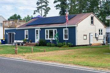 small residential home by the road with board siding on the facade and solar panels on the roof.