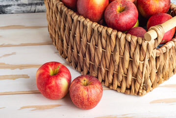Ripe, juicy apples in a wicker basket on a white wooden table.