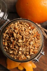 Jar of dried orange zest seasoning and fresh fruits on wooden table, flat lay