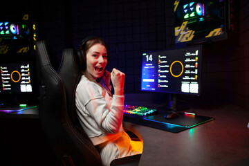 girl gamer sits at a computer and shouts at the monitor, crazy woman rejoices at victory in a computer club - obrazy, fototapety, plakaty