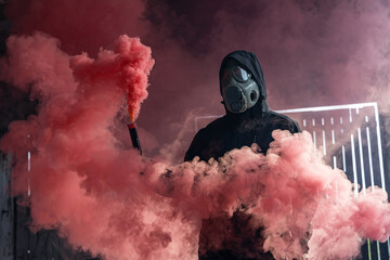 A man in gas mask holding a smoke bomb. Bright red colorful smoke. Old czechoslovakian gas mask...