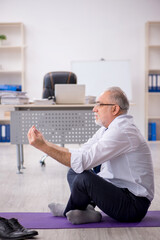 Old male employee doing sport exercises at workplace