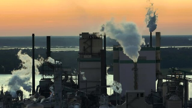 Aerial view of large factory with smokestack from production process polluting atmosphere at plant manufacturing yard. Industrial site at sunset