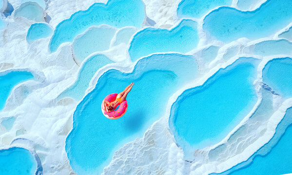 Travertine pools Pamukkale, Turkey travel. Woman swimming on pink inflatable donut in turquoise water, aerial top view