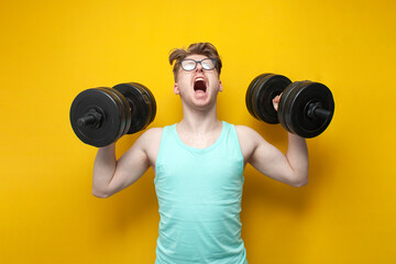 Fototapeta na wymiar young confident guy student lifts heavy dumbbells on a pink background, motivated nerd in glasses goes in for sports