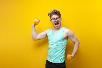 young non-athletic guy with glasses raises small dumbbells on a yellow background and screaming