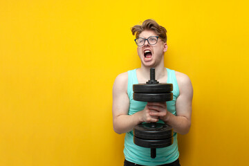 young confident guy student lifts heavy dumbbells on a pink background, motivated nerd in glasses...