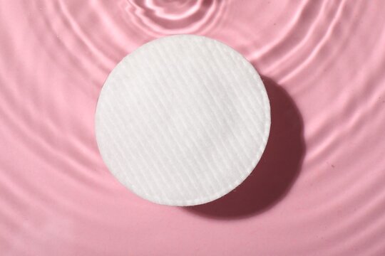 Cotton pad and micellar water on pink background, top view