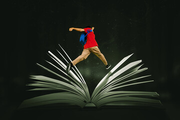 Male student jumping over a big open book