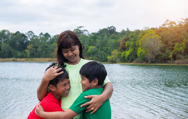Fototapeta na wymiar Happy family spending time outdoors hugging and enjoying the view of river. Mother with two kids.