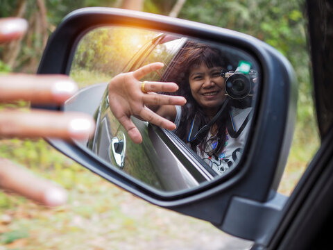 A woman holds a digital camera and takes a picture of herself smiling reflected in the car mirror.