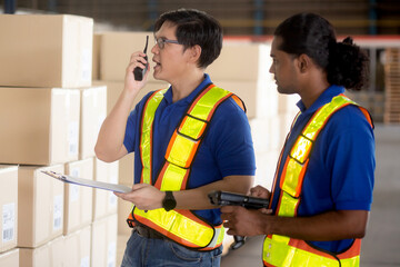 Supervisor young man standing using radio talking for instruction and planning while worker inspector cargo at distribution warehouse, logistic and depot for transportation, shipping and shipment.