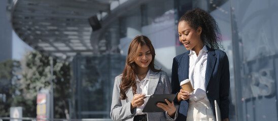 Two asia business women in conversation walking together on city street. Corporate colleagues...