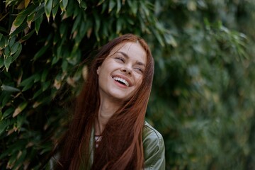 Portrait of happiness woman with red flying hair smile with teeth walking in the city in the park against a backdrop of green bamboo leaves, spring in the city