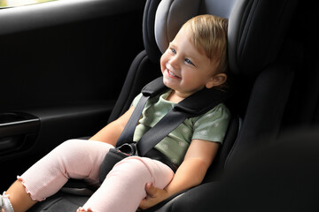 Cute little girl sitting in child safety seat inside car