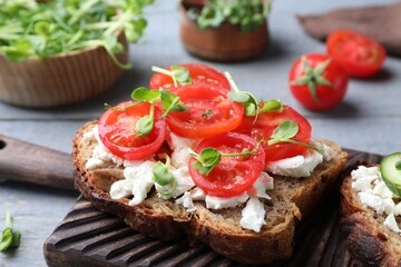 Fototapeta na wymiar Delicious sandwich with cherry tomatoes, microgreens and cheese on wooden board, closeup
