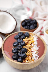Bowl of delicious fruit smoothie with fresh blueberries, granola and coconut flakes on white marble table