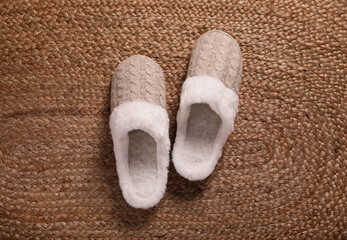 Pair of warm stylish slippers on wicker carpet, top view