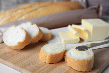 Tasty cut baguette with fresh butter on white table, closeup