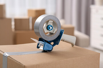 Dispenser with roll of adhesive tape on box indoors, closeup
