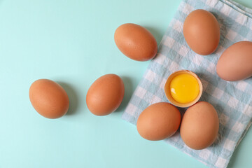 Cracked and whole chicken eggs with napkin on light blue background, flat lay