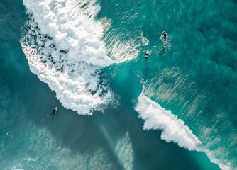 Surfers are seen from above in blue pristine ocean water
