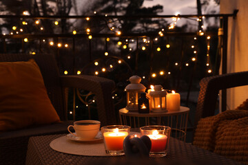 Beautiful view of garden furniture with pillow, soft blanket and burning candles at balcony