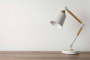 Stylish modern desk lamp on wooden table near white wall, space for text