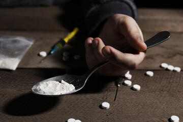Addicted man holding spoon with drugs at wooden table, closeup