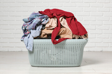 Laundry basket with clothes near white brick wall