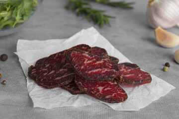 Slices of delicious beef jerky and spices on light grey table, closeup