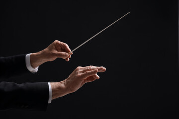 Professional conductor with baton on black background, closeup