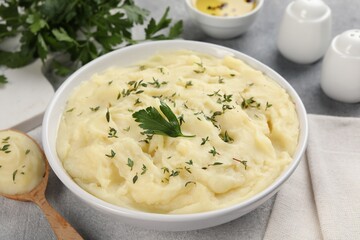 Bowl of tasty mashed potato, parsley, olive oil and pepper on grey marble table, closeup
