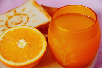 beautiful breakfast in the morning. bread toasts fried to crisp with the image of smiling sun on wooden plate, bright orange juice in yellow glass and half of orange close up. Selective focus