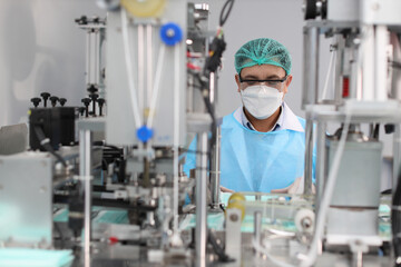 Fototapeta na wymiar Worker in personal protective equipment or PPE inspecting quality of mask and medical face mask production line in factory, manufacturing industry and factory concept.
