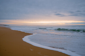 Obraz premium Wide sandy beach, stormy sea, and beautiful cloudy sky. Sunset over the sea, copy space for the text