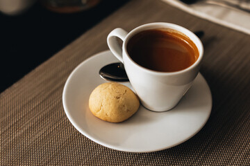 White cup of hot espresso coffee with a cookie on the table